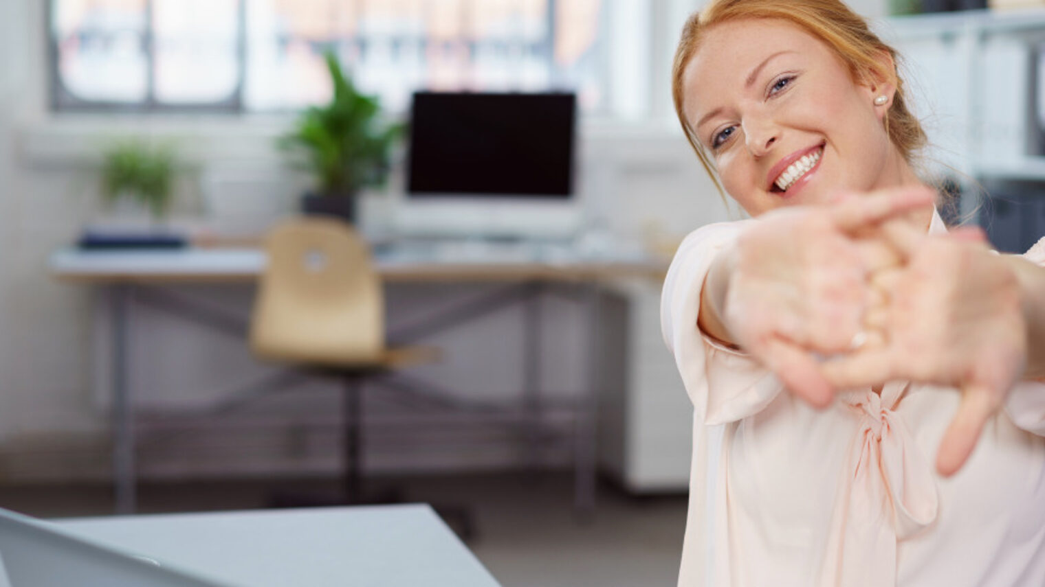 Frau im Büro am Tisch dehnt ihre Hände und Arme.
