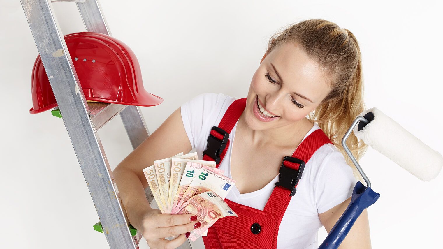 Eine Auszubildende im Handwerk mit Malerrolle, Helm und Leiter freut sich über eine Reihe von Geldscheinen.