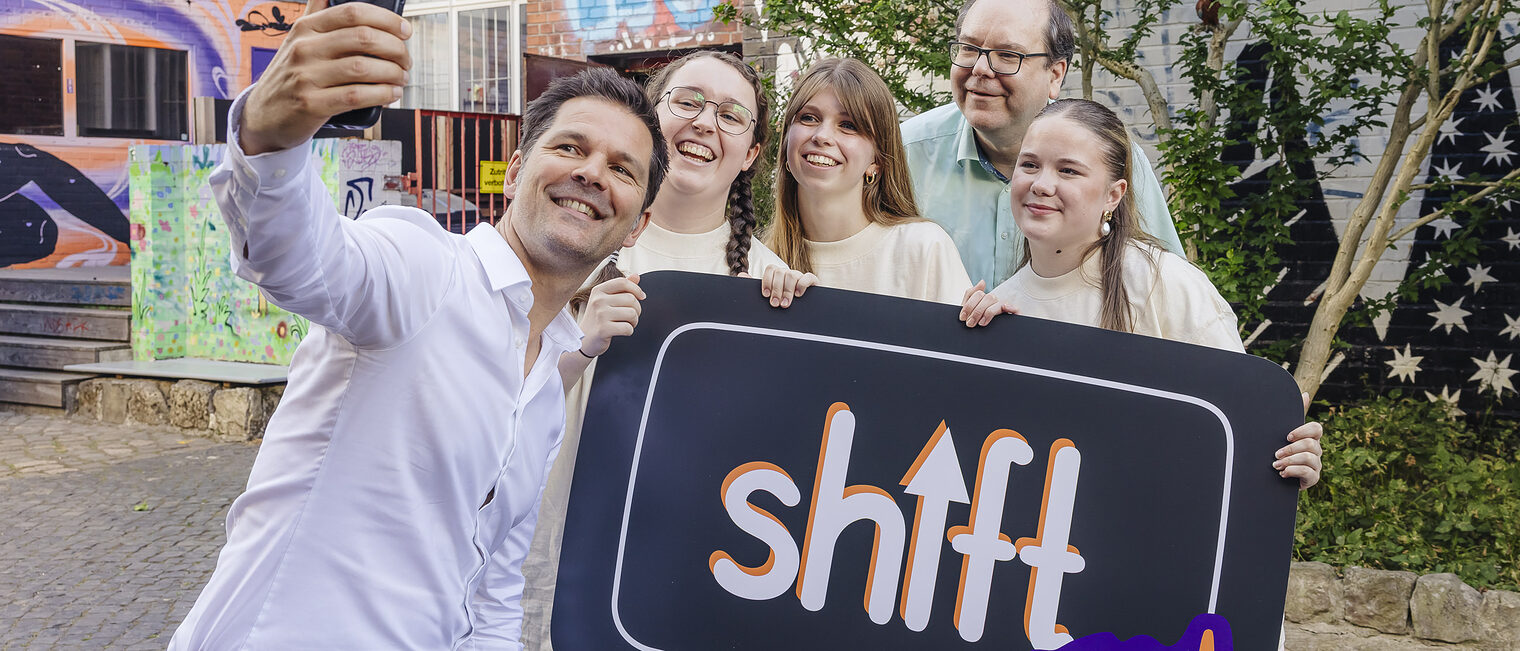 Regionspräsident Steffen Krach und Niedersachsens Umweltminister Christian Meyer machen gemeinsam mit Jugendlichen ein Selfie vor einem Plakat mit der Aufschrift ShiftNow.