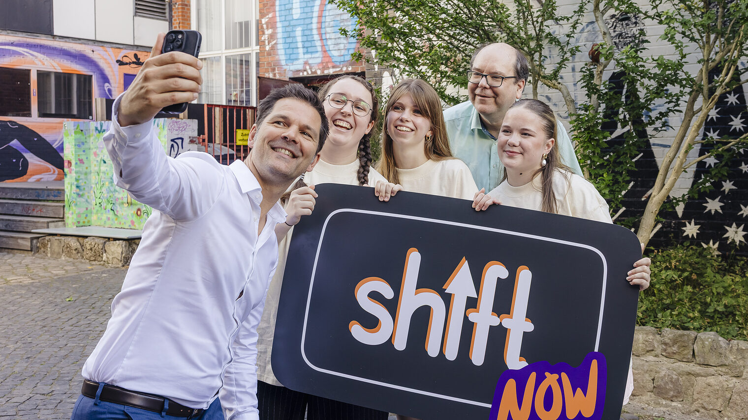 Regionspräsident Steffen Krach und Niedersachsens Umweltminister Christian Meyer machen gemeinsam mit Jugendlichen ein Selfie vor einem Plakat mit der Aufschrift ShiftNow.