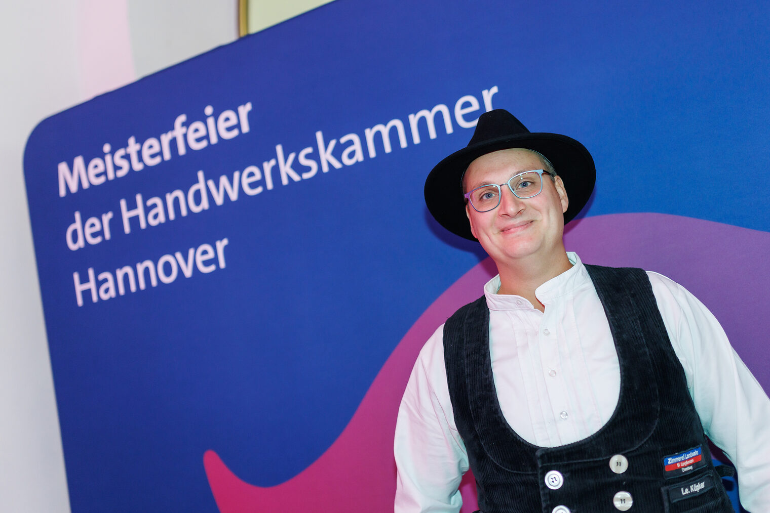 Porträt von Zimmerermeister Lennart Thamm vor Leinwand mit der Aufschrift Meisterfeier der Handwerkskammer Hannover.