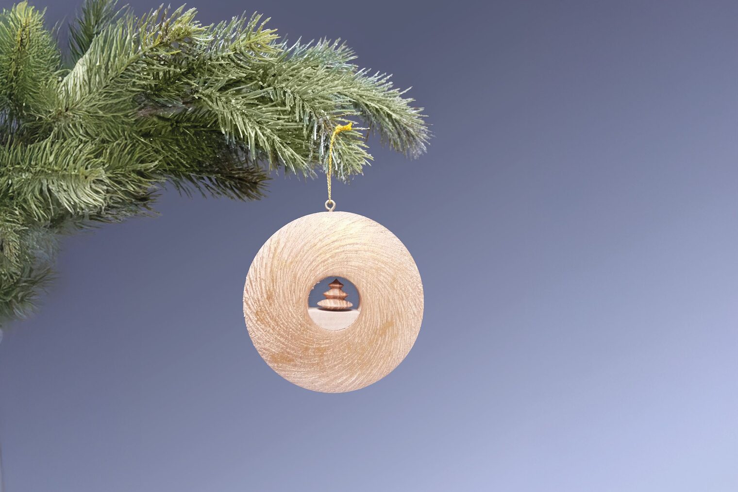 Runder Holzanhänger-Ring mit kleinem Weihnachtsbaum in der Mitte hängt an Tannenzweig.