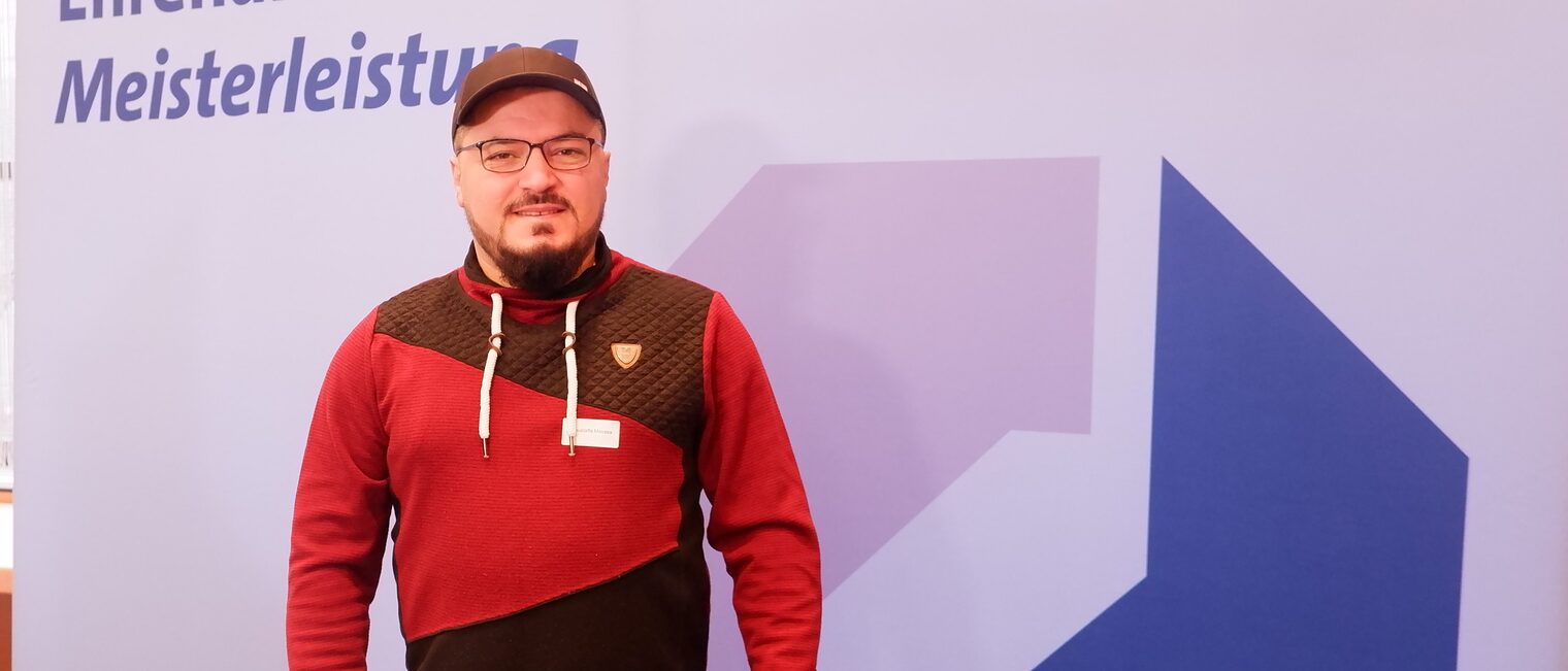Mustafa Moussa vor einer Leinwand mit der Aufschrift: Ehrenamt ist Meisterleistung.