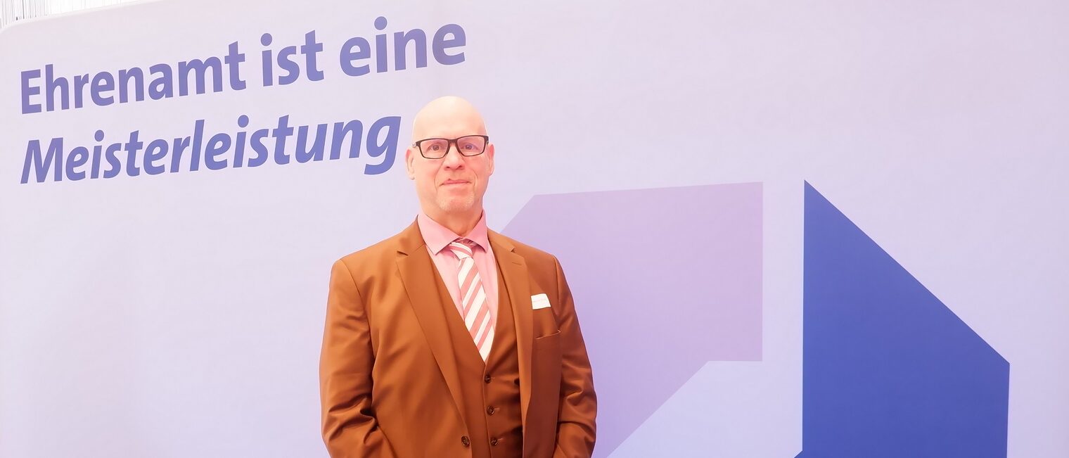 Frank-Joachim Weiß vor der Leinwand mit der Aufschrift Ehrenamt ist eine Meisterleistung