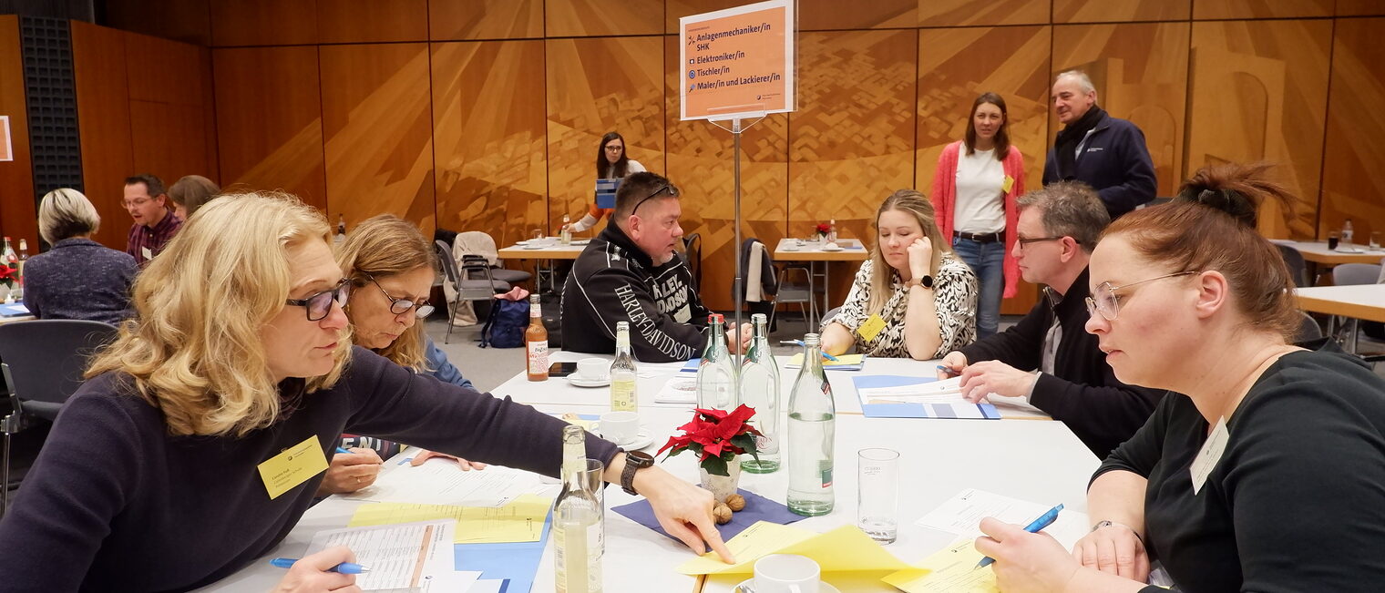 Sechs Menschen sitzen an einem Tisch und unterhalten sich.