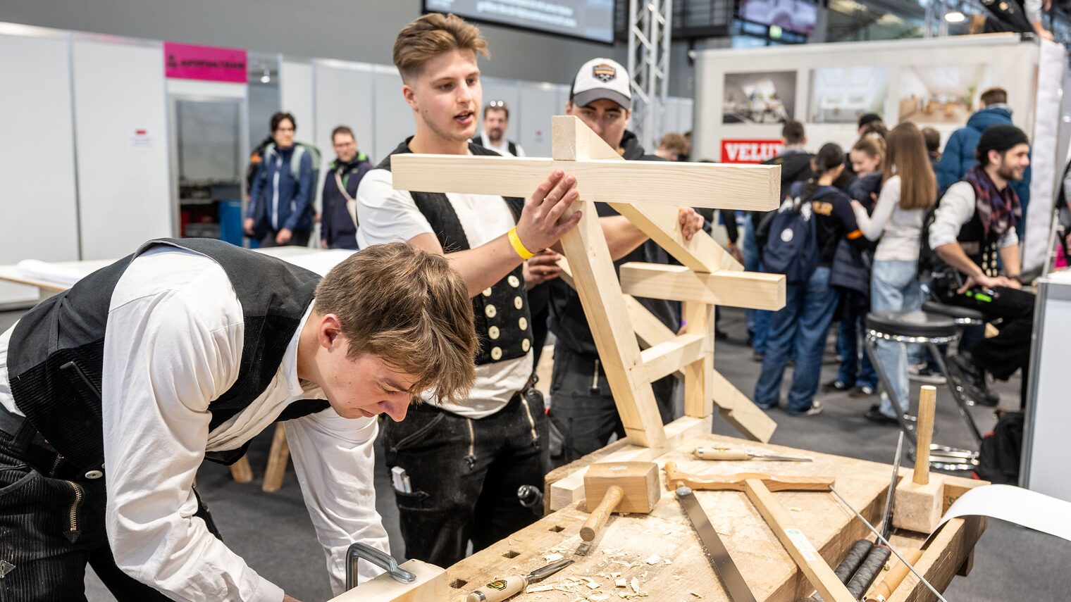 Zwei Zimmerer bauen an einem Objekt aus Holz bei der IHM in einer Messehalle.