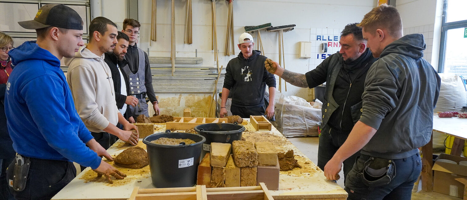 Fachausbilder im Maurerbereich Wolf Sonnet erklärt einer Gruppe Meisterschüler die Funktionsweise von Lehmbau. 