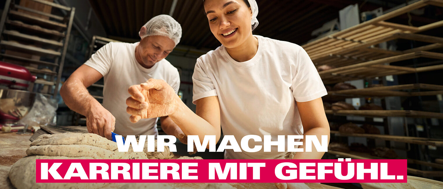 Bäcker und Bäckerin streuen Mehl auf Brot. 