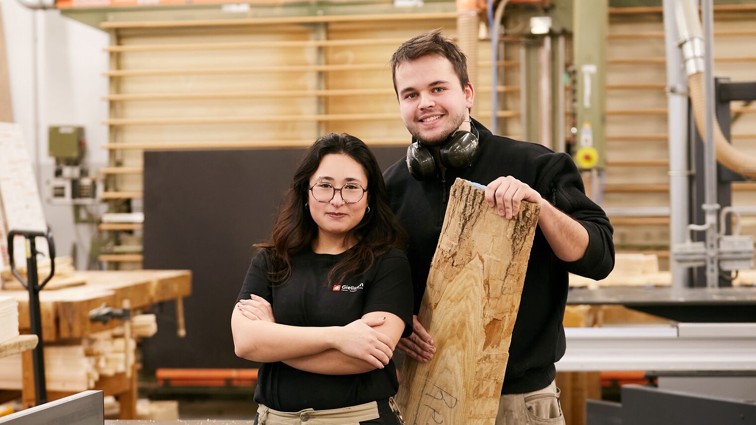 junge Frau und junger Mann nebeneinander in einer Tischlerwerkstatt.