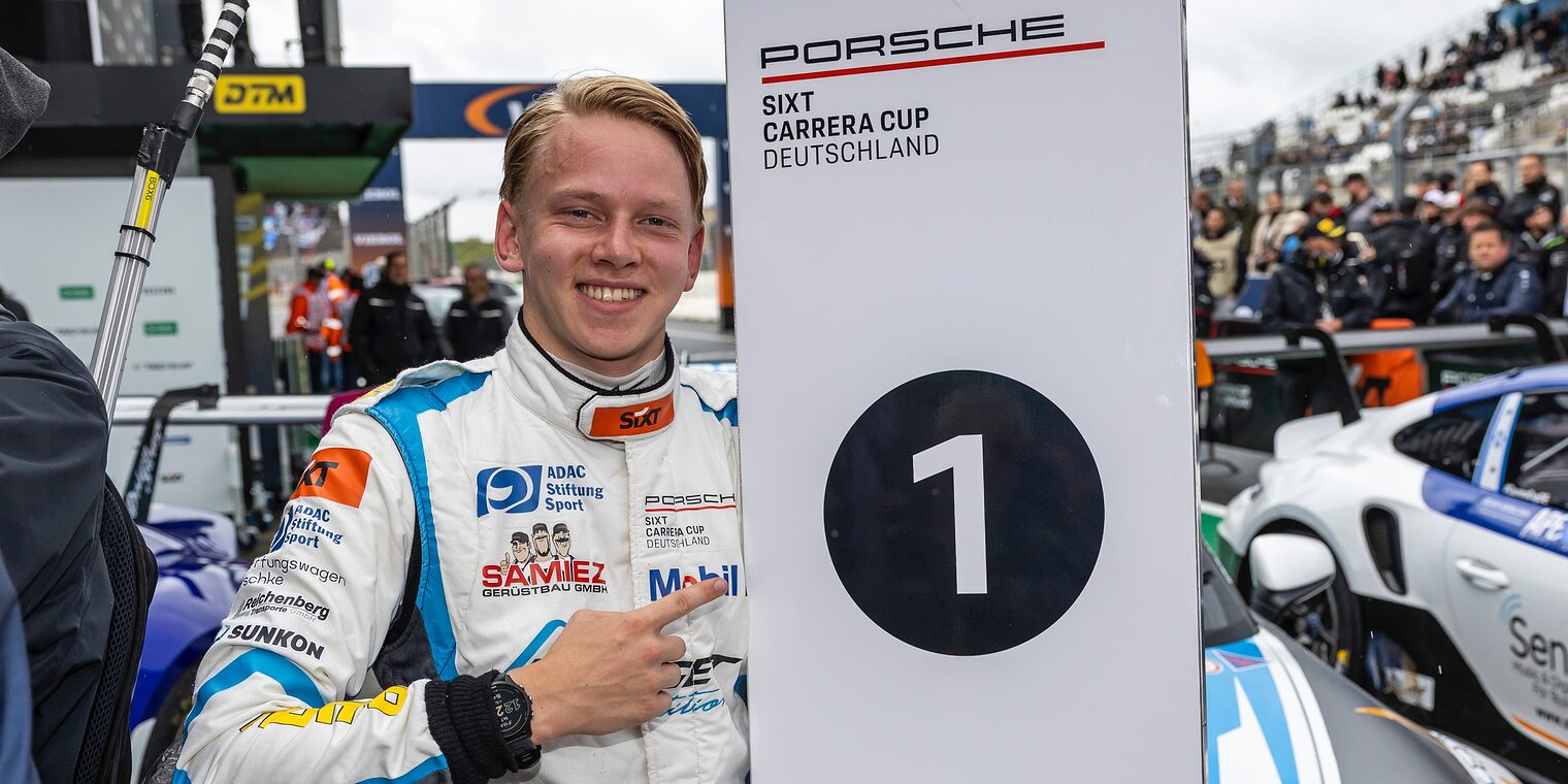 Janne Stiak am Rande der Rennstrecke zeigt auf ein Banner mit dem Aufdruck Nummer 1 beim PorscheCup.