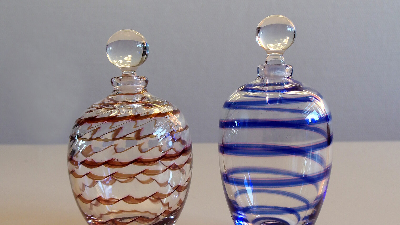 Zwei Parfümfläschchen aus Glas, eine mit roten Linien, eine mit blauen.