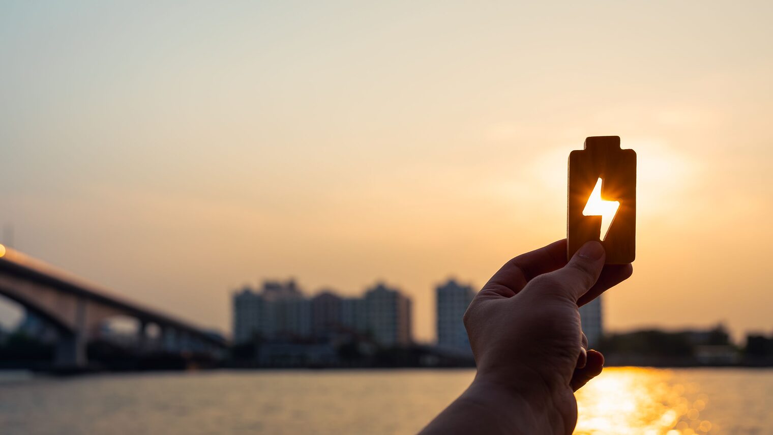 Stadtpanorama, Sonne, Hand hält Batterie mit Energiesymbol gegen Sonne