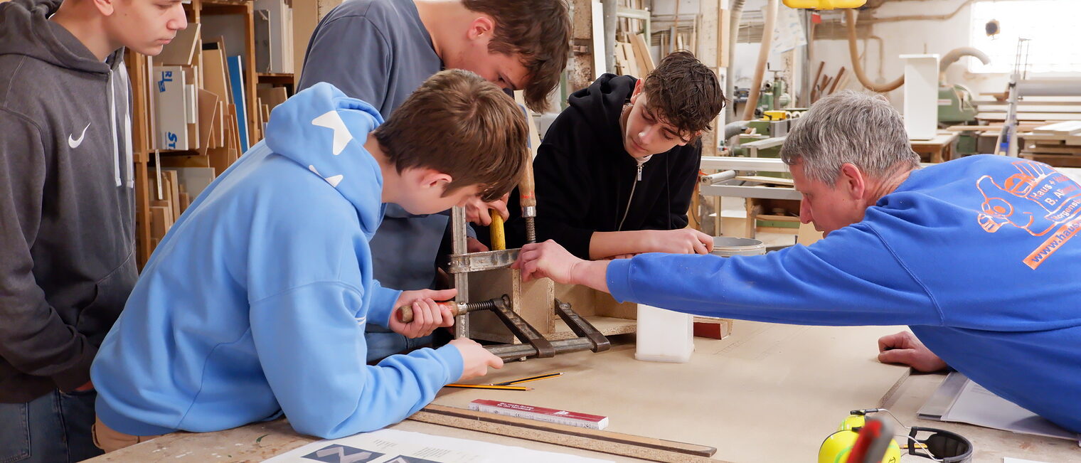 Schülerinnen und Schüler arbeiten in einer Tischlerei an einem Möbelstück.
