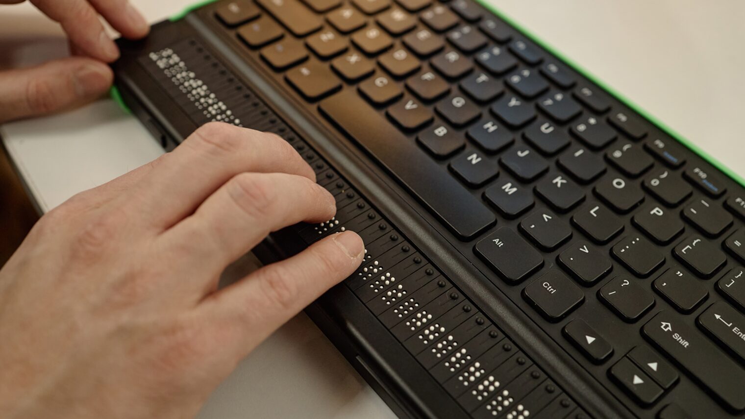 Person, die Braille-Schrift auf einer Tastatur liest.
